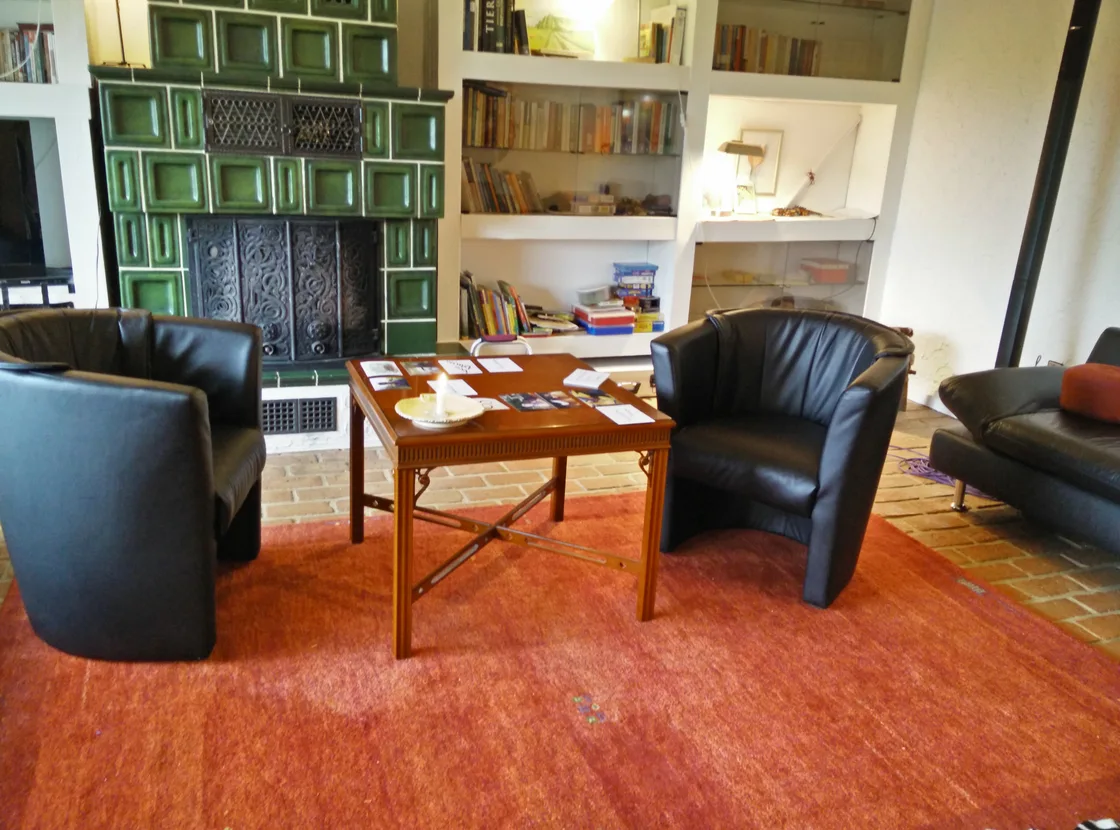 Sessel um einen kleinen Holztisch, Bücher und ein grüner Kachelofen im Praxisraum.